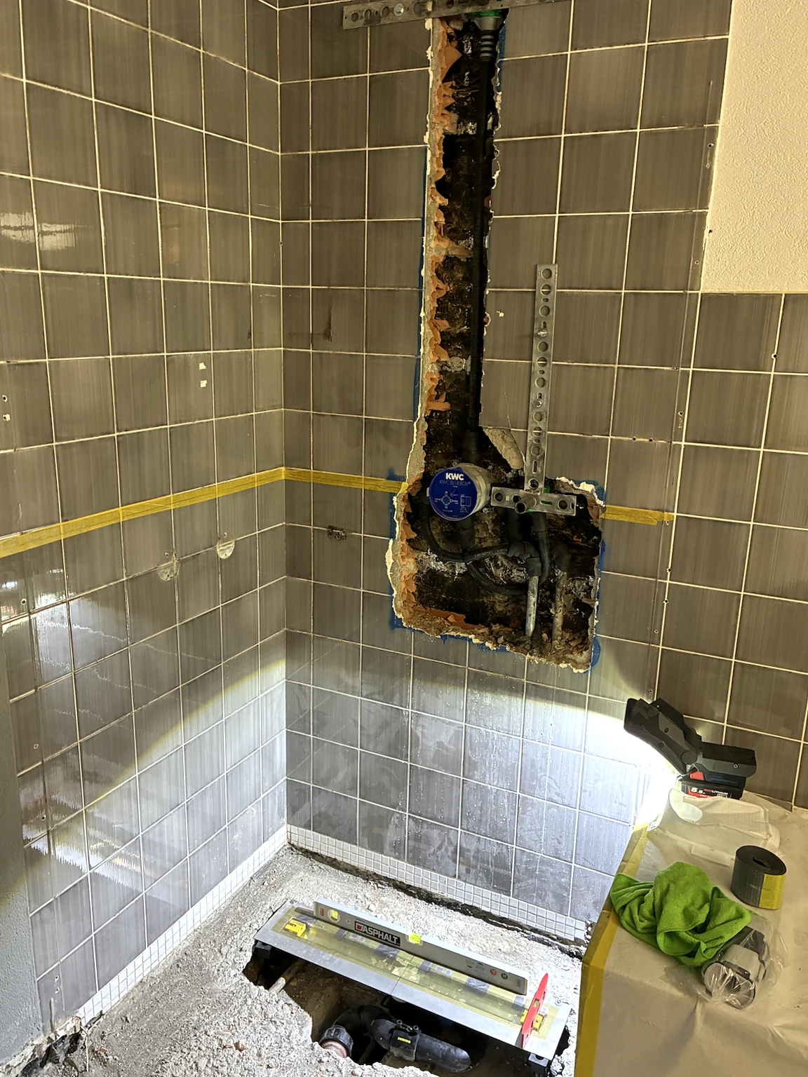 Freigelegte Wasserinstallation in einer gefliesten Badezimmerwand